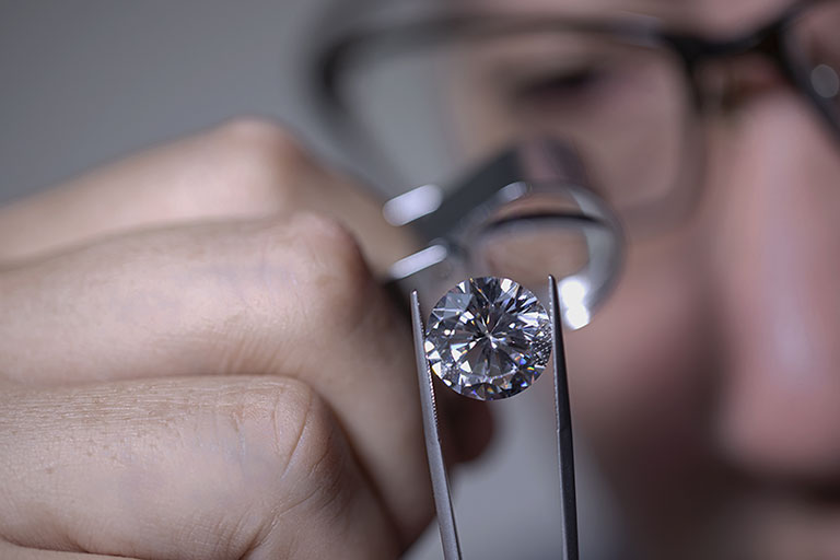 expertise d’un diamant sur papier ou non serti sur bijou par un spécialiste en gemmologie qui utilise une loupe professionnelle et une pince